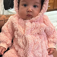 Alannah is registered to the contest to win money with this photo: baby, infant, pink, onesie, fluffy, hood, curly_hair, face, indoor, person, cute, soft_texture, hands, sitting, clothing, kitchen, background, cozy, portrait, child