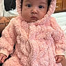 baby, infant, pink, onesie, fluffy, hood, curly_hair, face, indoor, person, cute, soft_texture, hands, sitting, clothing, kitchen, background, cozy, portrait, child