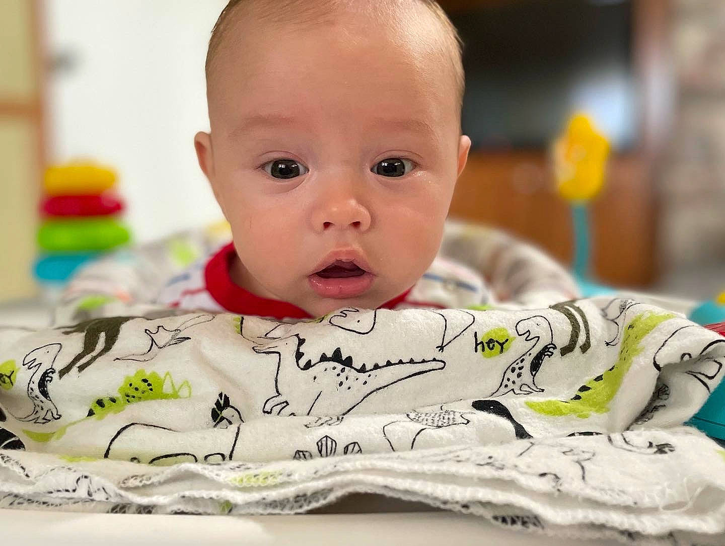 Colton is registered to the contest to win money with this photo: baby, baby_products, baby_toddler_clothing, bedding, cheek, child, comfort, font, fun, happy, linens, pattern, person, portrait_photography, room, sitting, sleeve, smile, surprise, t_shirt