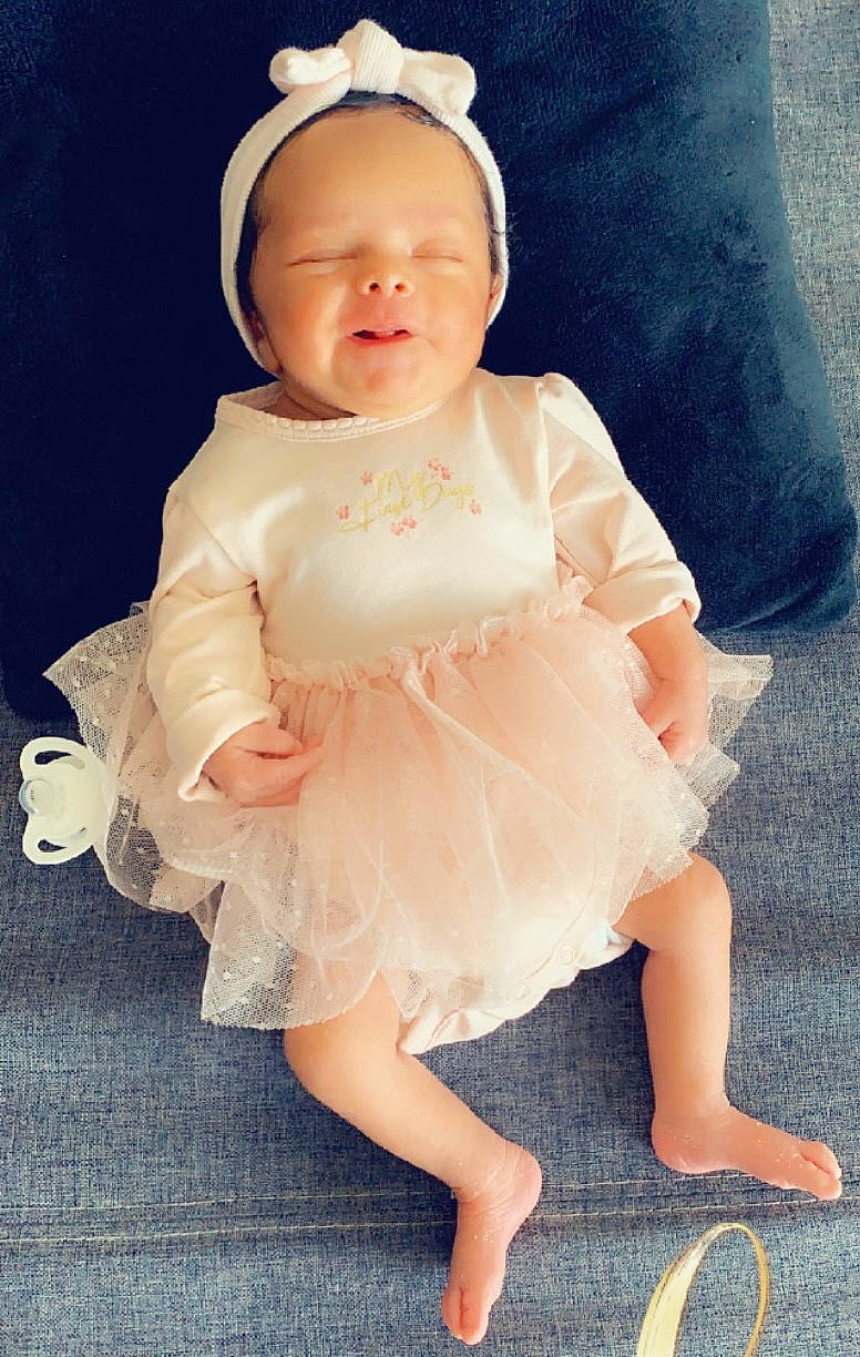 Kamila a rejoint le concours — aidez-le/la à gagner de superbes lots ! baby, baby_toddler_clothing, child, costume, day_dress, dress, embellishment, fashion_accessory, hair_accessory, happy, headpiece, human_leg, one_piece_garment, pattern, peach, person, pink, ruffle, sitting, sleeve