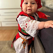 Selena a rejoint le concours — aidez-le/la à gagner de superbes lots ! toddler, child, red_headscarf, traditional_clothing, white_lace, standing, indoor, carpet, couch, curious_expression, face, person, cute, young_child, colorful_outfit, home_interior, soft_focus, floor, holding, portrait