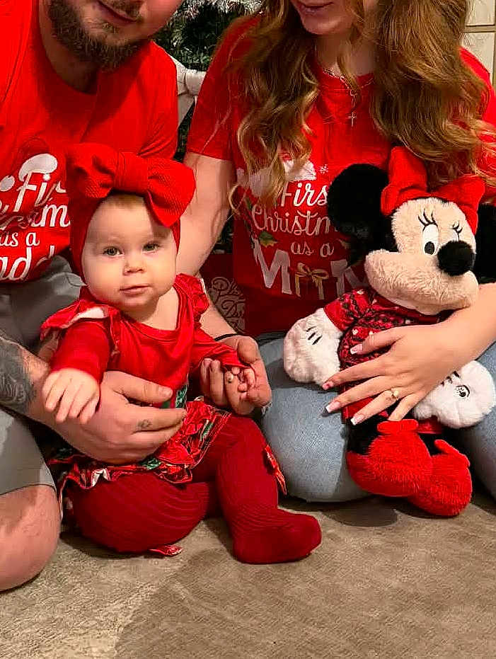 Selena participe au concours pour gagner de l'argent avec cette photo : baby, child, adult, family, christmas, holiday, red_clothing, bow, plush_toy, minnie_mouse, carpet, sitting, holding, smiling, indoor, person, casual, tshirt, jeans, tattoo