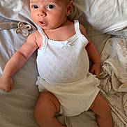 Blue is registered to the contest to win money with this photo: baby, infant, white_clothing, bed, pacifier, blanket, skin, head, face, eyes, arm, leg, hand, foot, lying_down, indoors, soft_lighting, expression, newborn, cute
