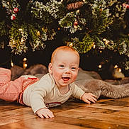 Owen joined the competition — help win amazing prizes! baby, child, smiling, lying_down, floor, wooden_floor, christmas_tree, holiday, festive, decorations, lights, pine_branches, red_hair, striped_pants, cream_sweater, indoors, happy, cute, seasonal, celebration