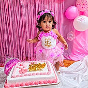 Ava joined the competition — help win amazing prizes! toddler, birthday, cake, pink, dress, flower_crown, balloons, streamers, celebration, party, child, happy, decorations, cake_topper, curious, indoors, standing, white, floor, festive