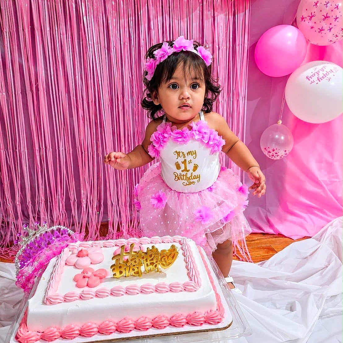 Ava joined the competition — help win amazing prizes! toddler, birthday, cake, pink, dress, flower_crown, balloons, streamers, celebration, party, child, happy, decorations, cake_topper, curious, indoors, standing, white, floor, festive