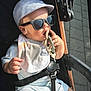 baby, sunglasses, cap, stroller, bib, teething_toy, sunlight, child, outdoor, cute, infant, clothing, hand, face, seatbelt, toy, summer, fashion, portrait, happy
