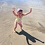 child, beach, sand, water, sunny, swimsuit, pink_cap, flamingo, shadow, smiling, joyful, summer, vacation, outdoor, playful, barefoot, shoreline, people, nature, holiday