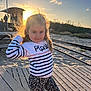 Inaya participe au concours pour gagner de l'argent avec cette photo : child, sunset, beach, boardwalk, curly_hair, striped_sweater, leggings, playful, outdoor, sand, railway_tracks, nature, smiling, person, sunlight, portrait, casual_clothing, young_girl, evening, fun