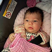 Emily is registered to the contest to win money with this photo: baby, infant, child, car_seat, blanket, pink, portrait, face, eyes, wide_eyed, sitting,  안전, harness, floral_clothing, indoor, cozy, soft_fabric, newborn, passenger, photography
