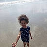 barefoot, beach, candid, child, curly_hair, dress, girl, hair, happy, ocean, outdoor, playing, polka_dot_dress, running, sand, screenshot, shoreline, smiling, water, waves