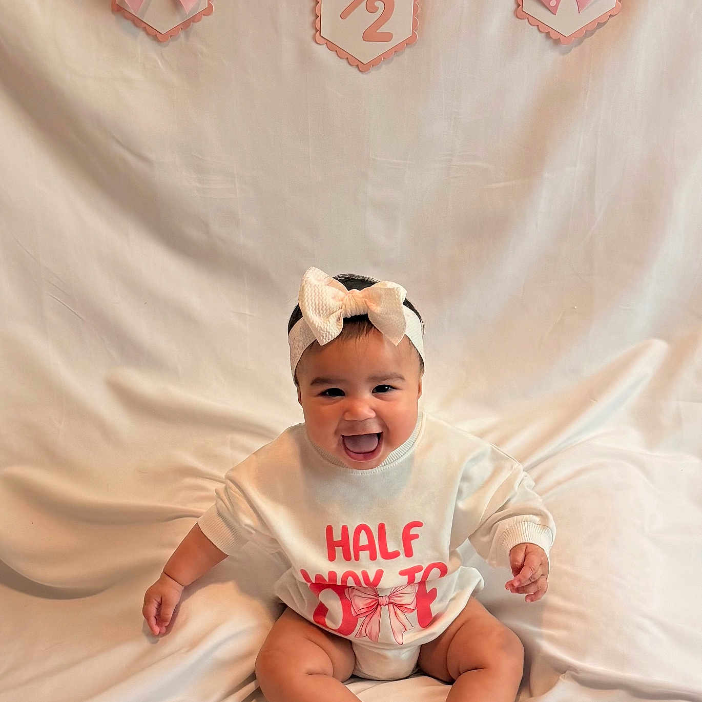 Alaya is registered to the contest to win money with this photo: baby, smiling, headband, bow, sweatshirt, pink, white_background, celebration, milestone, sitting, happy, infant, cute, child, portrait, indoors, fabric, clothing, feet, sock