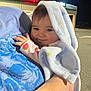 baby, blanket, child, cute, face, hand, holding, person, portrait, smile, strawberry, sleeve, night, parking_lot, shirt, blue, light, store_sign, outdoor, adult