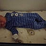 Skylar is registered to the contest to win money with this photo: baby, newborn, sleeping, infant, pajamas, blue_clothing, striped_clothing, crib, mattress, blanket, teddy_bears, nursery, indoors, lying_down, portrait, face, closed_eyes, resting, cozy, photograph
