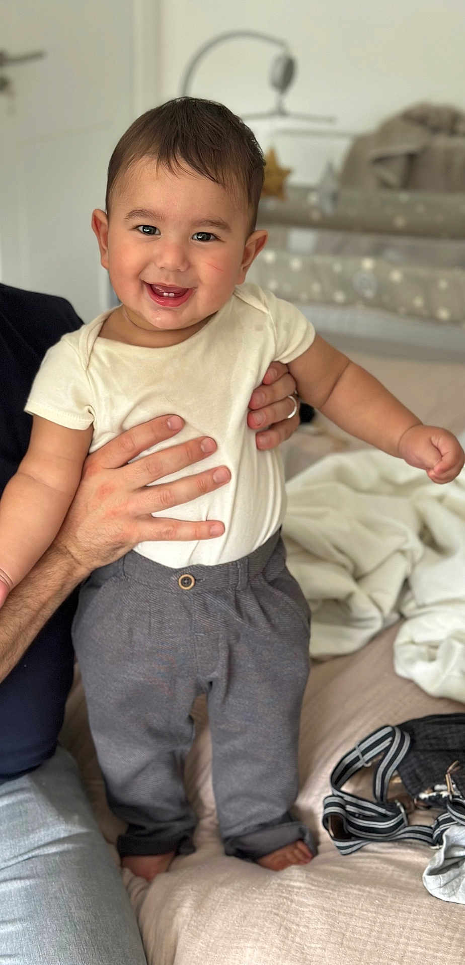 Owen joined the competition — help win amazing prizes! toddler, baby, child, smiling, standing, bed, clothing, pants, shirt, adult_hand, indoor, person, happy, cute, portrait, home, furniture, blanket, baby_gear, comfort