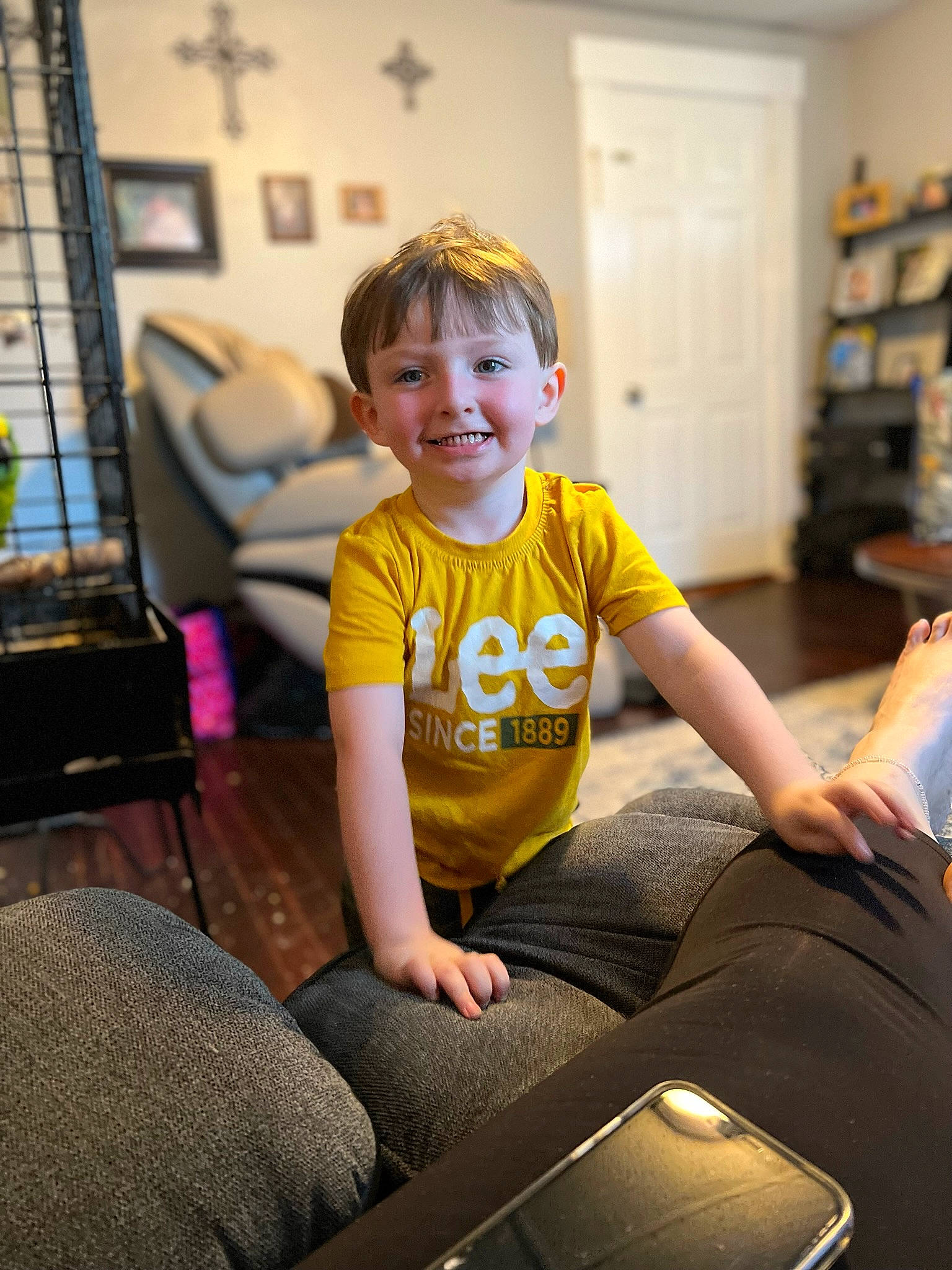 Christian is registered to the contest to win money with this photo: child, comfort, computer_keyboard, door, floor, flooring, fun, happy, joy, knee, lap, leisure, living_room, person, shelf, shorts, sitting, smile, standing, t_shirt