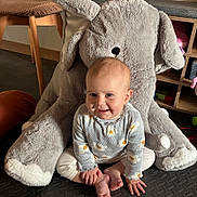 Stella participe au concours pour gagner de l'argent avec cette photo : baby, child, smile, sitting, plush_toy, elephant, indoor, floor_mat, clothing, toy, furniture, wooden_chair, shelf, foot, hand, happy, person, cute, playful, cozy