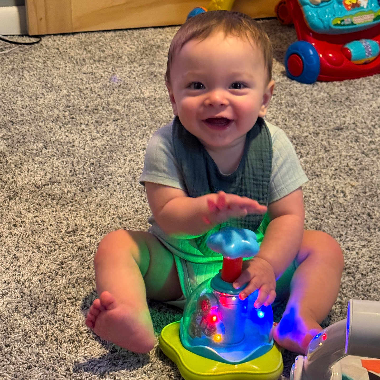 Sven is registered to the contest to win money with this photo: baby, carpet, child, clothing, colorful, cute, floor, furniture, hand, happy, indoors, infant, light, person, playtime, sitting, smiling, toy, walker, young_child