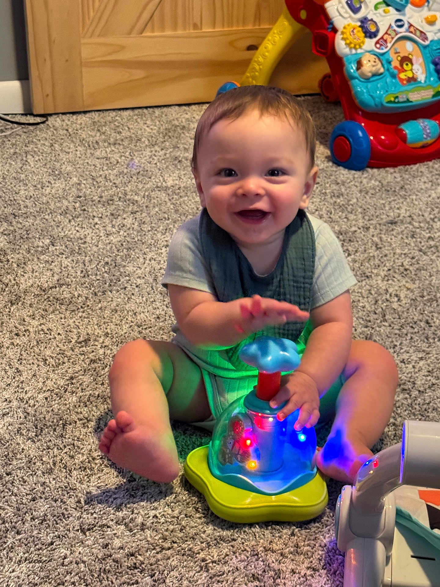Sven is registered to the contest to win money with this photo: baby, infant, carpet, toy, light, colorful, smiling, child, indoors, playtime, floor, walker, clothing, person, happy, cute, furniture, young_child, sitting, hand
