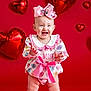 baby, toddler, child, smiling, bow, heart_balloon, valentine, pink, dress, sneakers, studio, portrait, standing, happy, clapping, red_background, ribbon, conversation_hearts, cute, playful