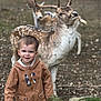animal, antlers, brown_jacket, casual_clothing, child, cute, daylight, deer, dirt, fence, forest, grass, jeans, nature, outdoor, portrait, smiling, toddler, wildlife, young_child