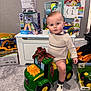 toddler, child, toy_tractor, john_deere, plaid_bow, indoor, carpet, toys, boxes, sweater, shoes, curious, baby, playroom, gift, vehicle, plastic_toy, floor, young_child, portrait