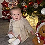 baby, child, christmas_tree, ornaments, lights, carpet, holiday, decorations, teddy_bear, toy, socks, shoes, coat, indoor, festive, smiling, face, person, seasonal, celebration