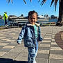 Sahas is registered to the contest to win money with this photo: toddler, child, denim_jacket, patchwork_jeans, sneakers, outdoor, waterfront, palm_trees, sunny, blue_sky, bench, cyclist, bicycle, urban, sidewalk, smiling, person, daytime, casual_clothing, nature
