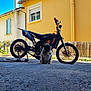 pug, dog, motorcycle, bike, vehicle, yellow_wall, outdoor, sunny, shadow, asphalt, window, building, fence, pet, animal, sitting, daylight, road, handlebars, wheels