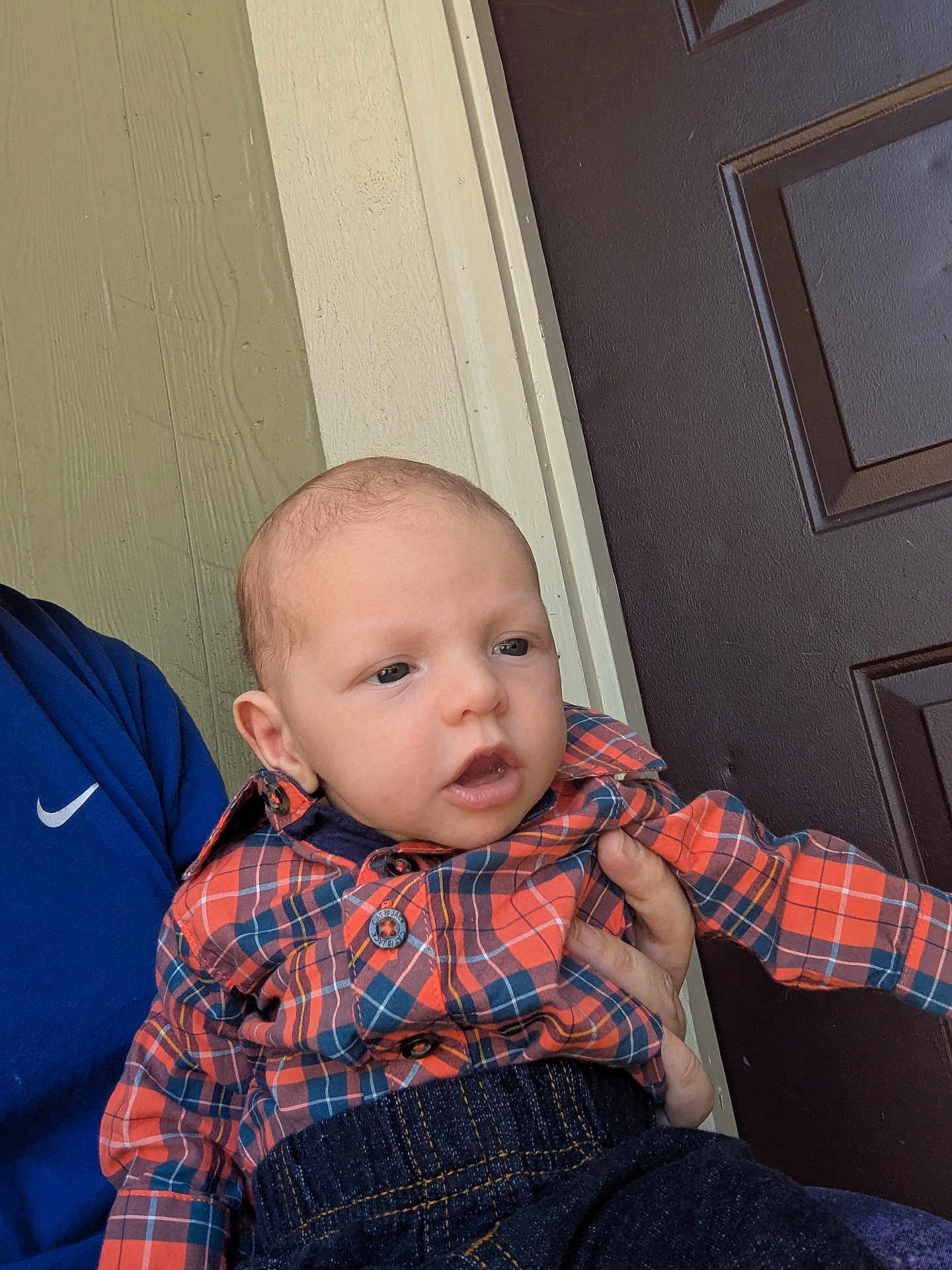 Gary is registered to the contest to win money with this photo: baby, child, plaid_shirt, orange, blue, person, infant, denim, door, hand, portrait, casual_clothing, indoor, curious_expression, holding, young_child, toddler, face, skin, head
