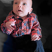 Gary is registered to the contest to win money with this photo: baby, infant, child, plaid_shirt, clothing, portrait, curious, eyes, face, hands, seated, dark_background, casual_wear, young_child, person, indoor, cute, expression, small_hands, newborn
