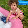 toddler, child, curly_hair, smiling, inflatable_pool, foam, grass, backyard, swimsuit, play, outdoor, basketball_hoop, summer, water_play, happy, cute, fun, daytime, person, young_child