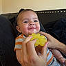 baby, child, teether, hand, smile, drool, striped_shirt, indoor, person, face, infant, happy, couch, black_fabric, skin, head, holding, yellow, closeup, comfort