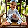 baby, child, smiling, blue_headband, bow, striped_clothing, wooden_chair, porch, outdoor, greenery, milestone_card, happy, feet, hands, face, sitting, cute, infant, natural_light, wood