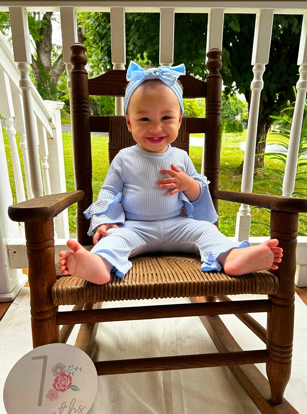 Mariposa joined the competition — help win amazing prizes! baby, child, smiling, blue_clothing, headband, wooden_chair, porch, outdoor, greenery, grass, tree, happy, cute, infant, feet, toes, natural_light, wood, sitting, portrait