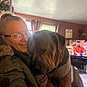 casual_clothing, companion, cozy, curtains, dog, furniture, glasses, home, hug, indoor, living_room, man_on_tv, natural_light, pet, portrait, smile, television, wall_art, window, woman