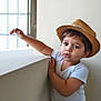 toddler, child, hat, straw_hat, white_shirt, denim_jeans, indoor, window, natural_light, curious, leaning, portrait, young_child, casual_clothing, cute, expression, short_hair, person, baby, standing