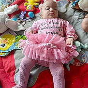 Joy participe au concours pour gagner de l'argent avec cette photo : baby, pink_tutu, tights, headband, play_mat, toys, stuffed_animal, book, indoor, child, infant, clothing, laying_down, cute, serious_expression, colorful, soft_toys, floor, young_child, portrait