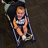 Jaxson joined the competition — help win amazing prizes! baby, child, stroller, smiling, sitting, indoor, floor, carpet, portrait, infant, blue_clothing, sleeveless_shirt, shoes, feet, harness, wheels, transportation, happy, face, photograph
