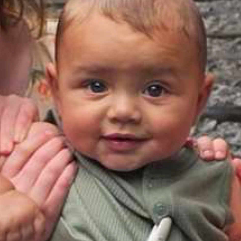 Jaxson is registered to the contest to win money with this photo: baby, infant, child, portrait, face, eyes, smiling, curious, indoor, close_up, person, hands, adult, support, clothing, green_outfit, pacifier, necklace, head, photography