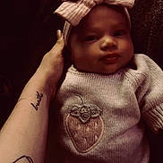 Tenley is registered to the contest to win money with this photo: baby, infant, knitted_sweater, strawberry_patch, headband, bow, tattoo, arm, hand, cozy, soft_texture, portrait, child, cute, indoors, person, wearing, clothing, newborn, resting
