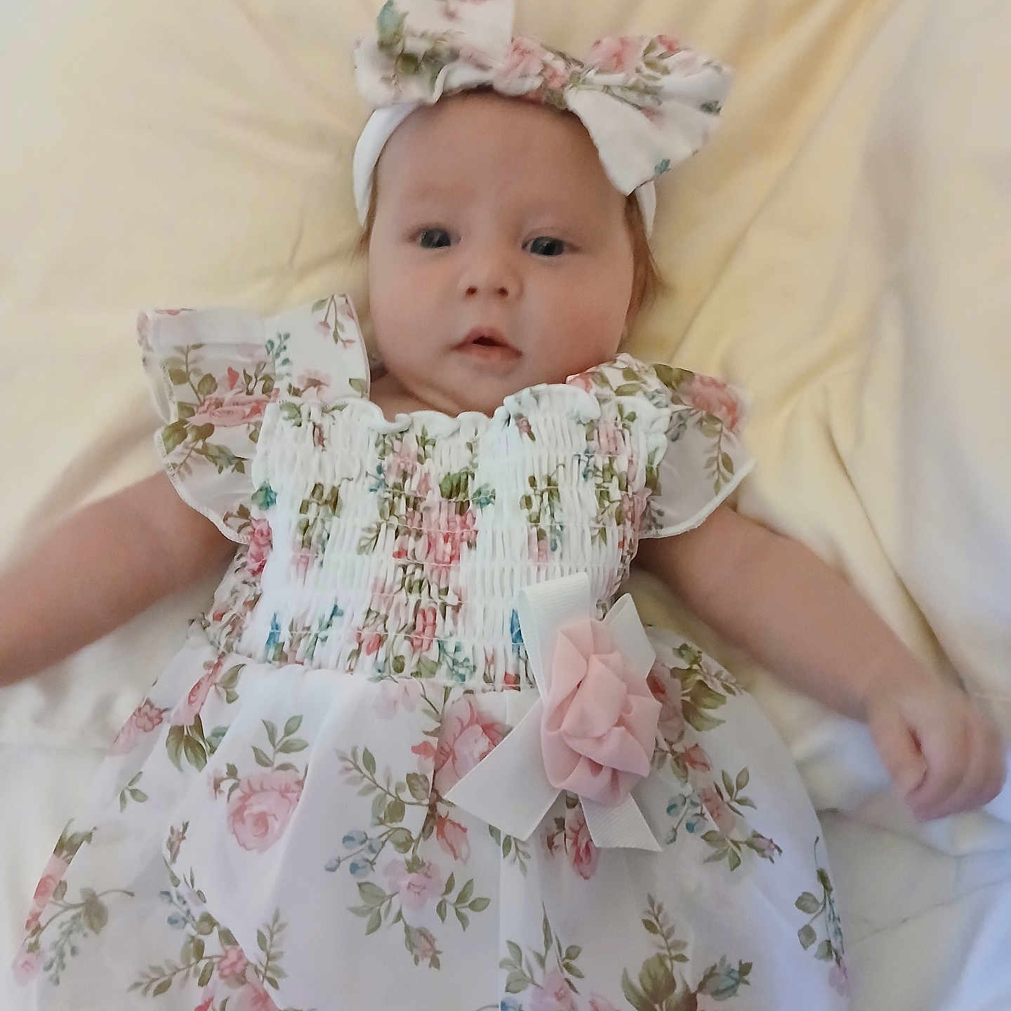 Atheana is registered to the contest to win money with this photo: baby, infant, child, floral_dress, headband, flower, blanket, soft, lying_down, cute, portrait, smile, young_child, person, indoors, skin, face, arm, hand, fabric