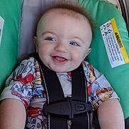 Michael is registered to the contest to win money with this photo: baby, smiling, car_seat, blue_eyes, child, clothing, straps, safety_harness, cute, infant, seat, happy, face, head, toddler, patterned_shirt, hair, skin, indoor, closeup