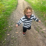 Kristain joined the competition — help win amazing prizes! black_pants, casual_clothing, child, curly_hair, daylight, dirt, grass, greenery, happy, leaves, nature, outdoor, path, playful, running, shoes, smiling, striped_sweater, toddler, trees