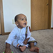 Harshavardhan joined the competition — help win amazing prizes! toddler, child, indoor, carpet, door, wall, white_clothing, traditional_clothing, gold_trim, sitting, playing, green_bowl, happy, smiling, barefoot, person, young_child, curious, home, floor