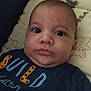 baby, infant, face, portrait, cushion, teddy_bear, clothing, blue_shirt, text_on_clothing, lying_down, indoors, child, cute, young, skin, head, expression, person, closeup, soft_toys