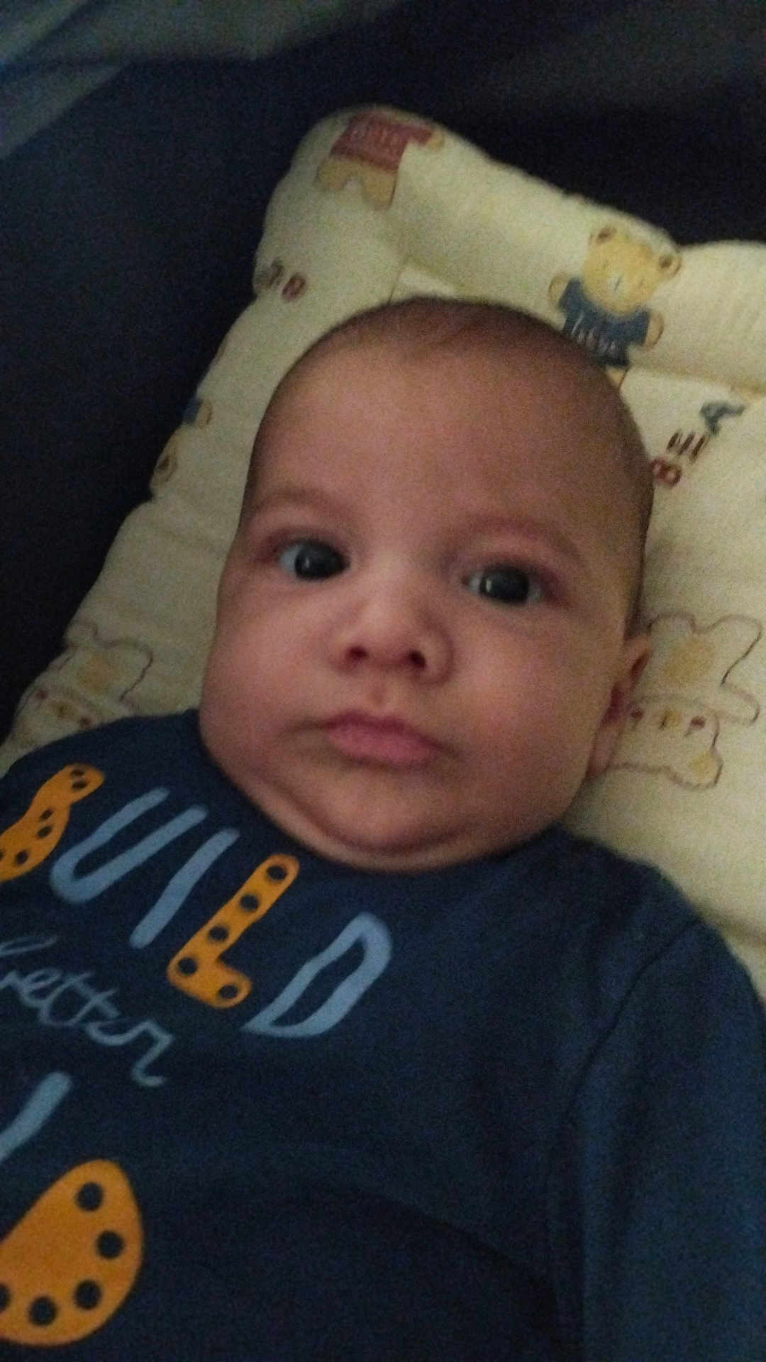 Adem a rejoint le concours — aidez-le/la à gagner de superbes lots ! baby, infant, face, portrait, cushion, teddy_bear, clothing, blue_shirt, text_on_clothing, lying_down, indoors, child, cute, young, skin, head, expression, person, closeup, soft_toys