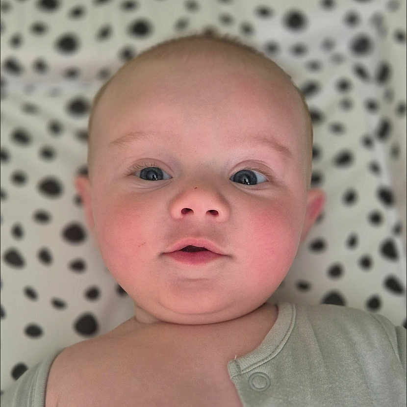 Sidney joined the competition — help win amazing prizes! baby, blanket, child, closeup, clothing, cute, expression, eyes, face, head, indoors, infant, laying, onesie, pattern, portrait, skin, soft, spot, young