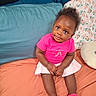 toddler, child, pink_shirt, pink_shoes, skirt, bed, pillow, blue_pillow, floral_pillow, orange_bedspread, curly_hair, cute, indoors, portrait, seated, looking_up, smiling, skin, person, young_child