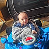 baby, infant, child, face, portrait, sitting, walker, toy, blue, blanket, gray, clothing, indoors, living_room, furniture, carpet, steering_wheel, curious, baby_gear, photograph